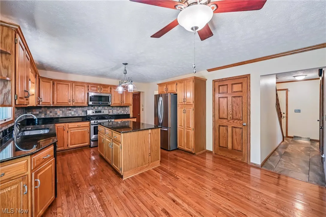 Kitchen featuring appliances with stainless steel finishes, a sink, a kitchen island, wood finished floors, and backsplash