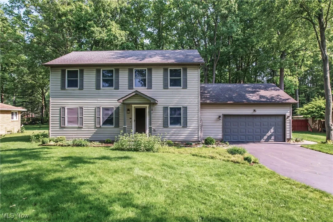 Colonial inspired home with driveway, an attached garage, a front yard, a shingled roof, and view of scattered trees