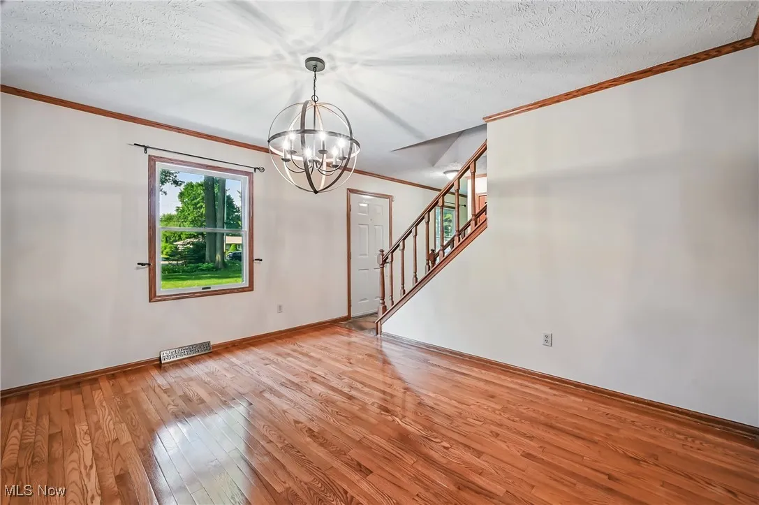Dining room featuring a chandelier, ornamental molding, light wood finished floors, stairway, and a textured ceiling