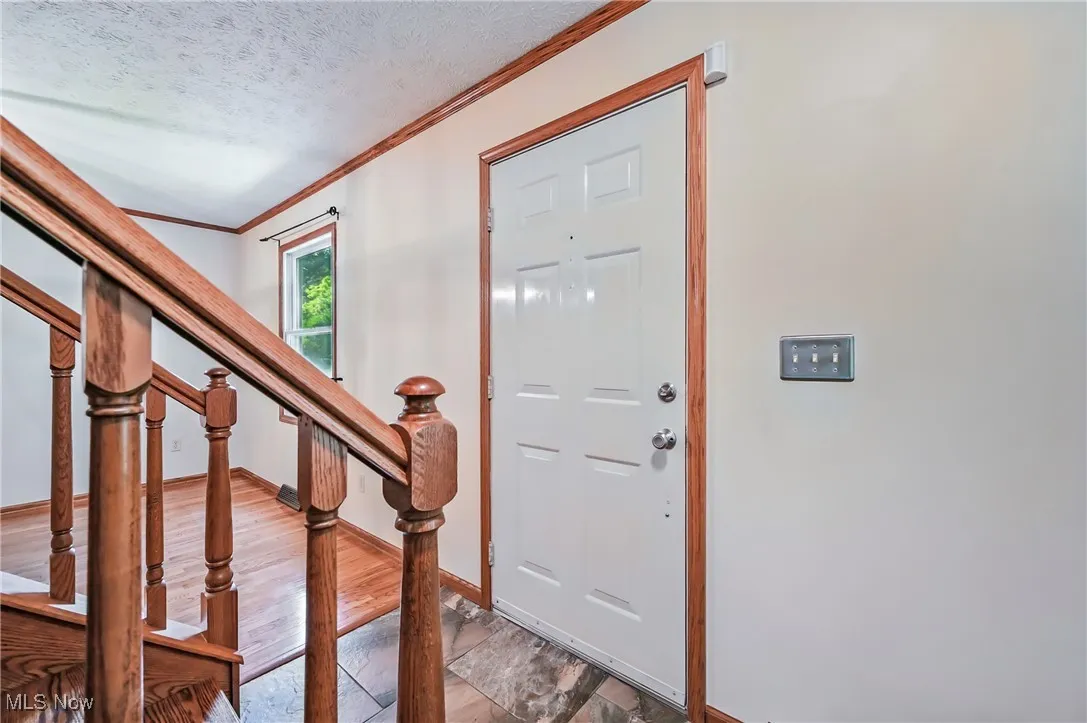 Entryway featuring crown molding, a textured ceiling, wood finished floors, baseboards, and stairway