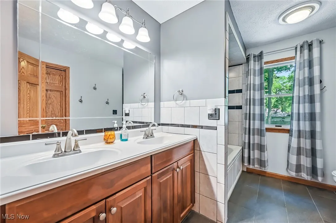 Full bathroom with tile walls, double vanity, shower / tub combo, tile patterned flooring, and toilet