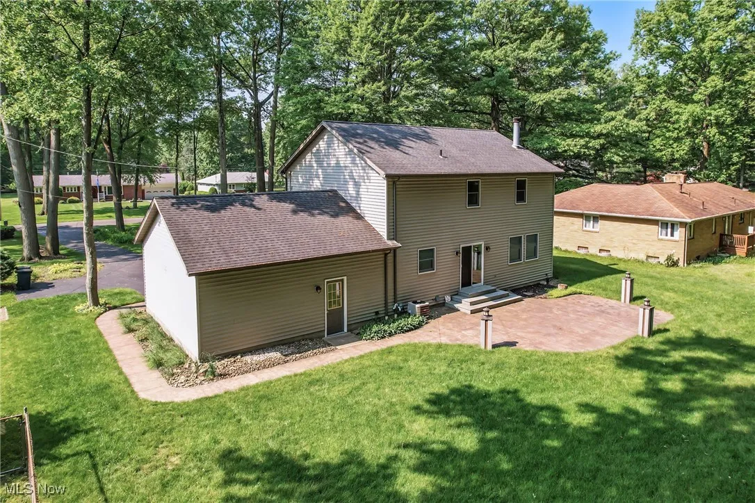 Rear view of property featuring a shingled roof, a yard, a patio area, and view of wooded area