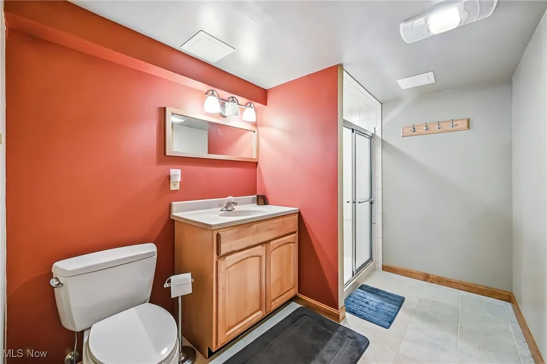 Full bath featuring vanity, a shower stall, toilet, and baseboards in basement