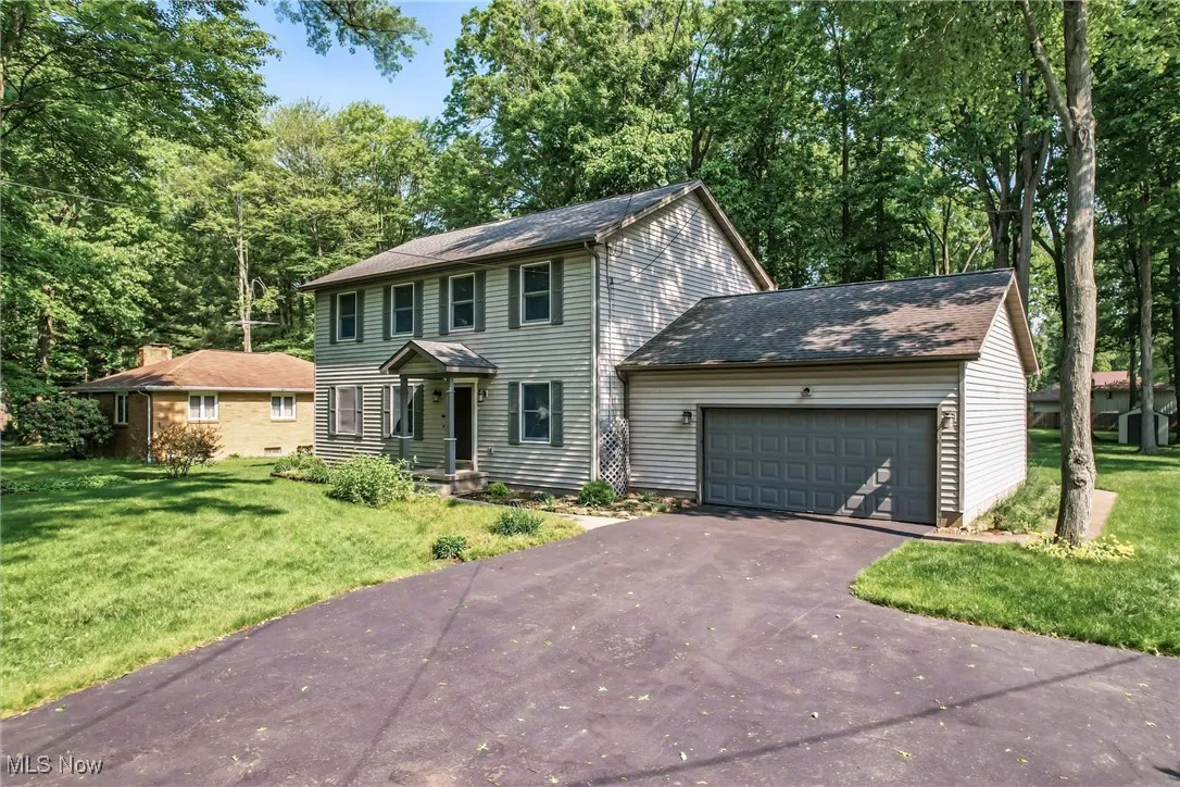 Colonial house with asphalt driveway, an attached garage, and a front lawn