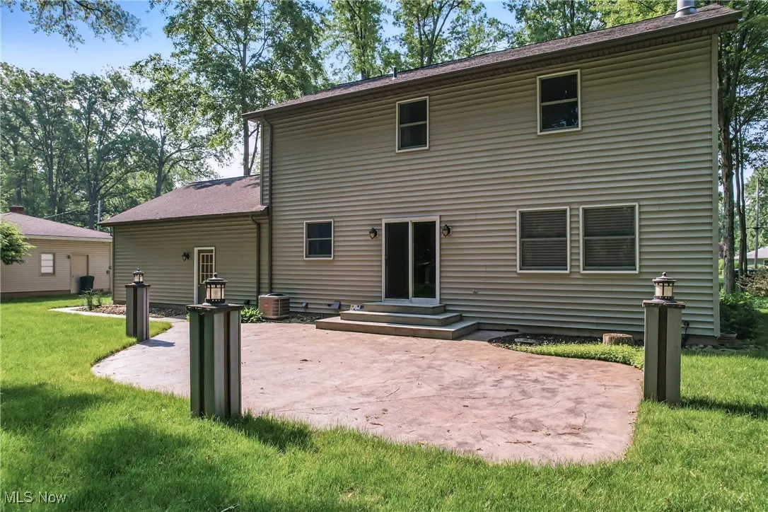 Rear view of property featuring a patio area, a lawn, entry steps, and a shingled roof