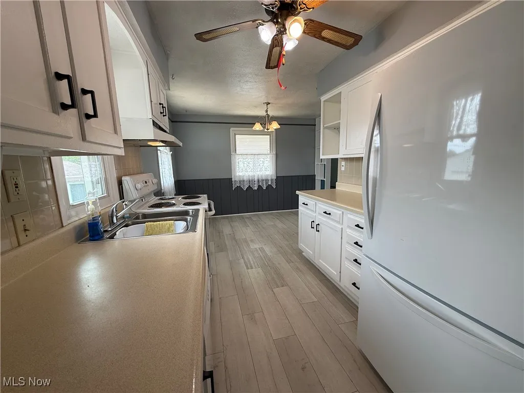 Kitchen with white appliances, wainscoting, under cabinet range hood, a ceiling fan, and light wood-style floors