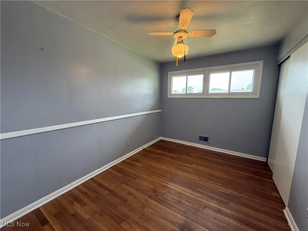 Unfurnished room featuring wood-type flooring, baseboards, a textured ceiling, and a ceiling fan