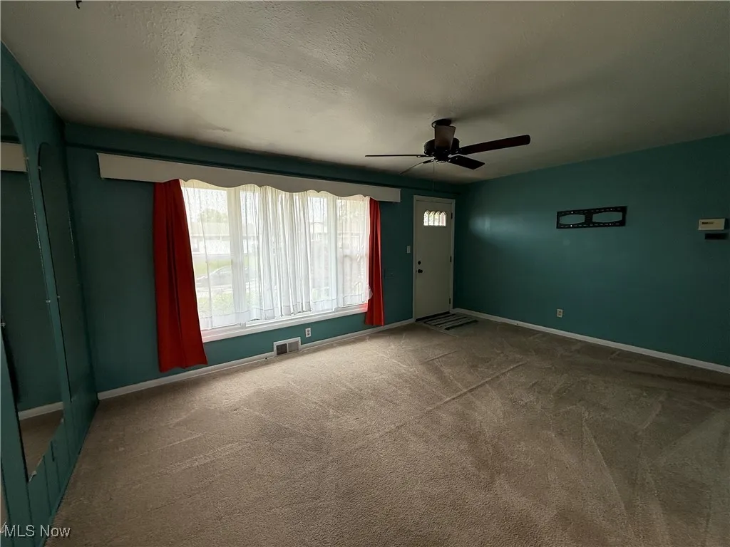 Carpeted spare room featuring ceiling fan and baseboards