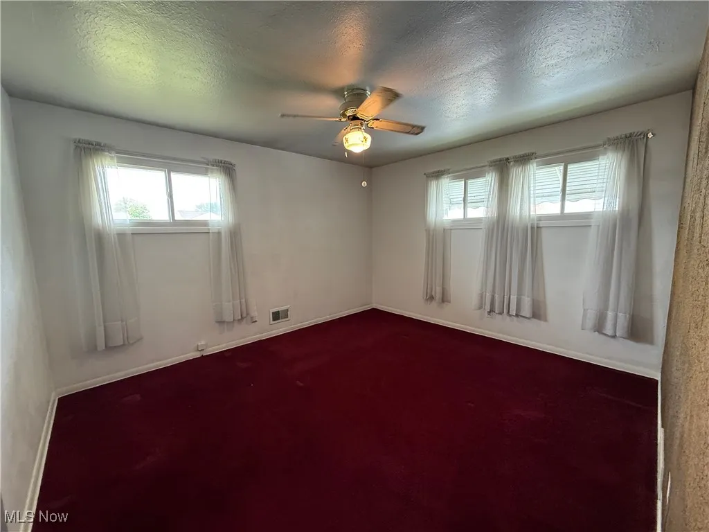 Unfurnished room featuring a ceiling fan, baseboards, a textured ceiling, and dark carpet