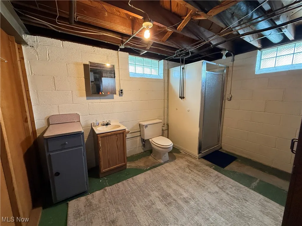 Bathroom with a stall shower, toilet, vanity, and unfinished concrete floors