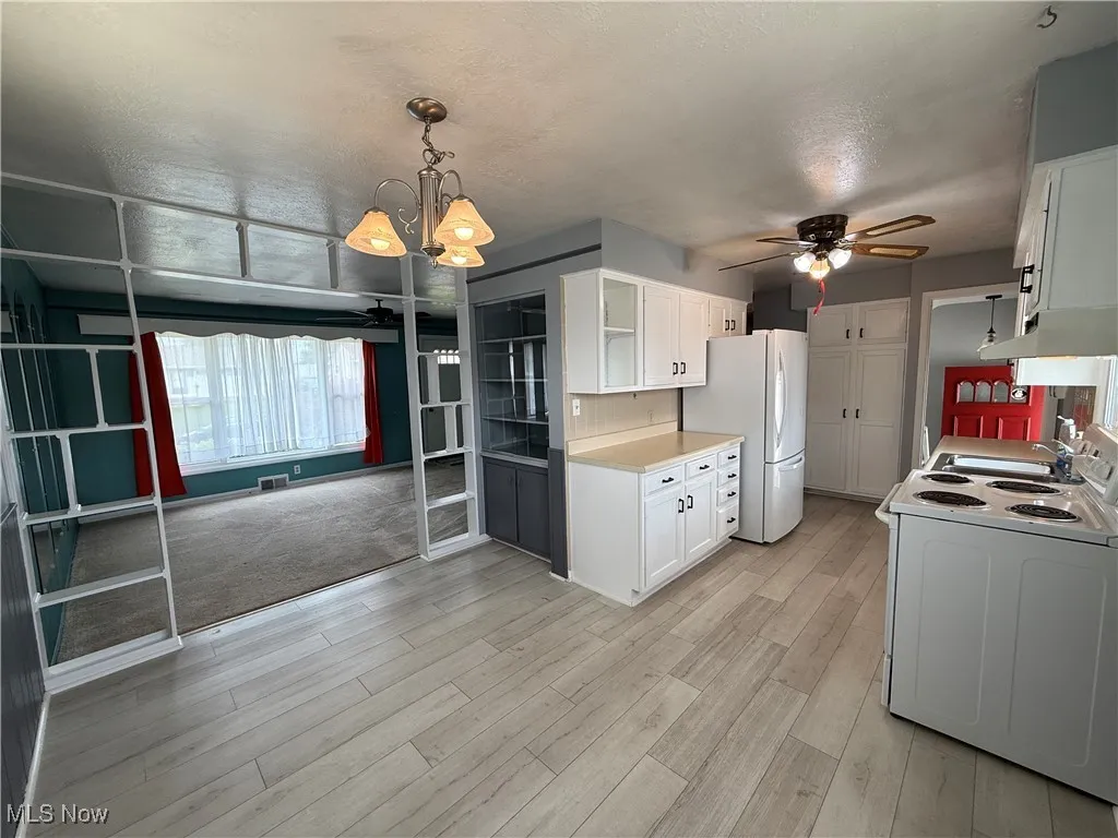 Kitchen featuring white appliances, ceiling fan, white cabinets, a chandelier, and light countertops