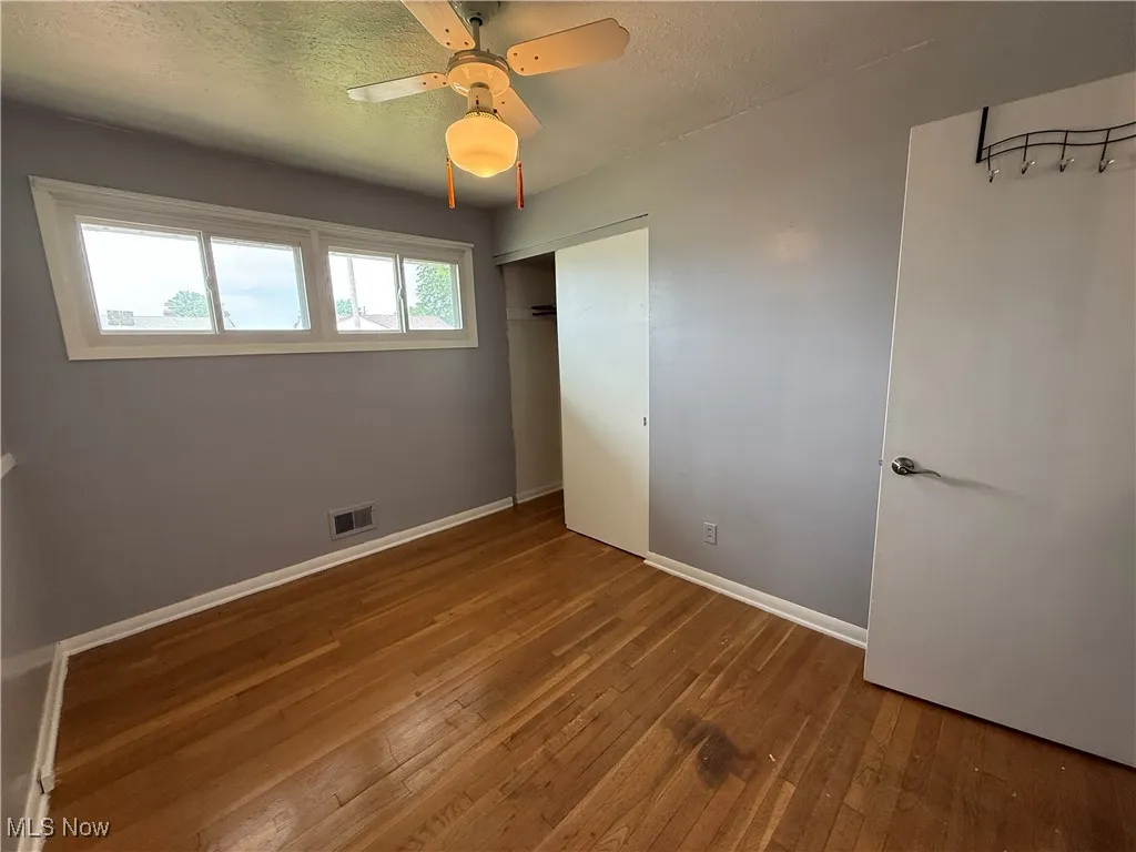 Unfurnished bedroom with hardwood / wood-style flooring, baseboards, a closet, a ceiling fan, and a textured ceiling
