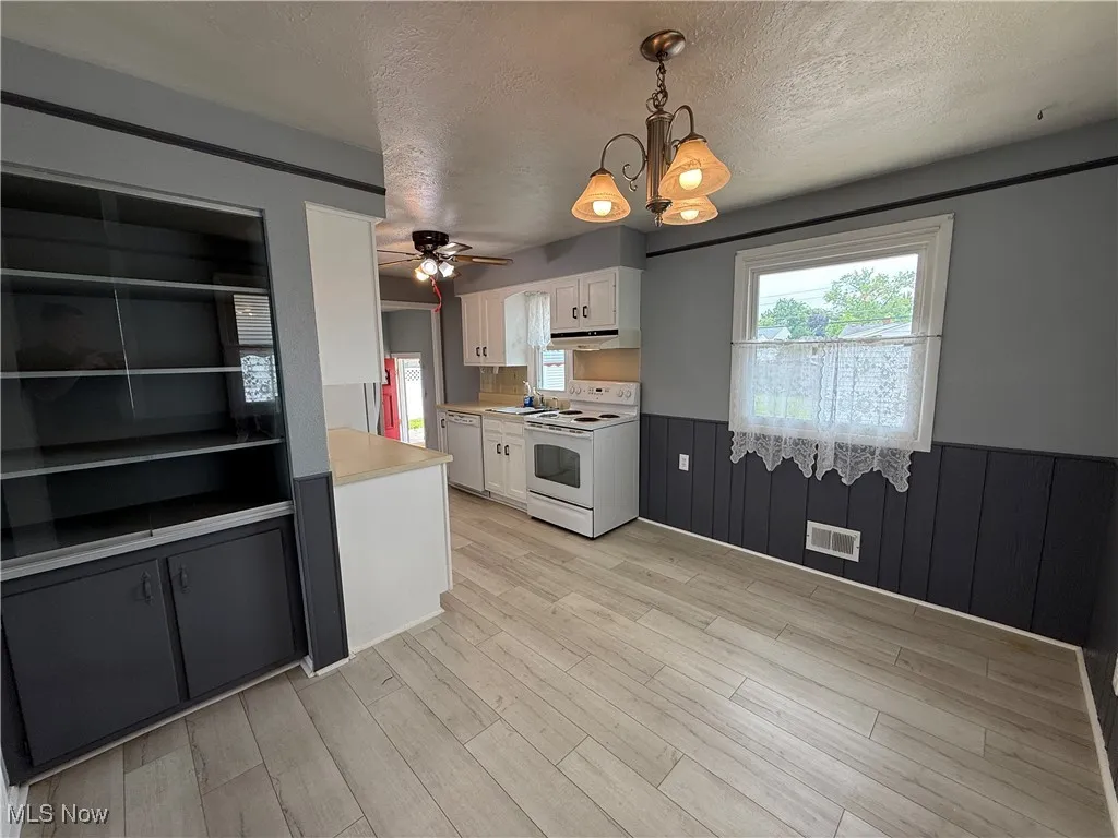 Kitchen with white appliances, wainscoting, white cabinetry, light countertops, and a chandelier