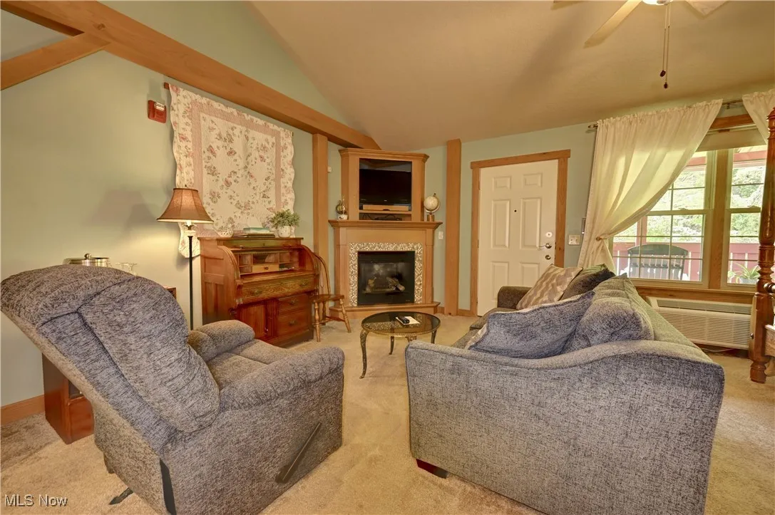 Carpeted living room featuring vaulted ceiling, ceiling fan, a fireplace, and a wall unit AC