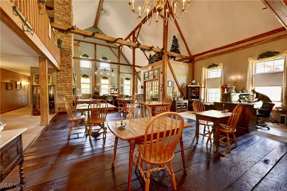 Dining space featuring high vaulted ceiling, hardwood / wood-style flooring, a chandelier, and beam ceiling
