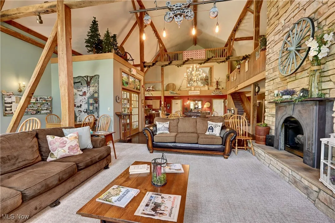 Carpeted living room featuring a chandelier, high vaulted ceiling, beamed ceiling, a fireplace, and stairs