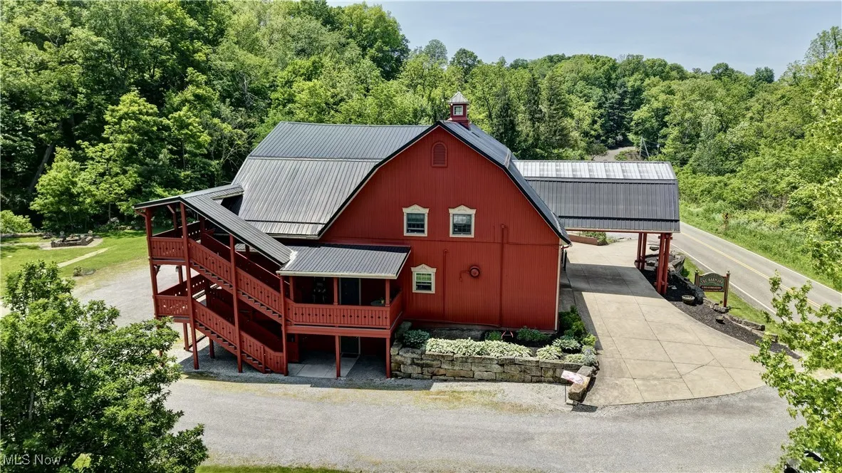 Back of house featuring an attached carport, concrete driveway, stairway, metal roof, and a view of trees