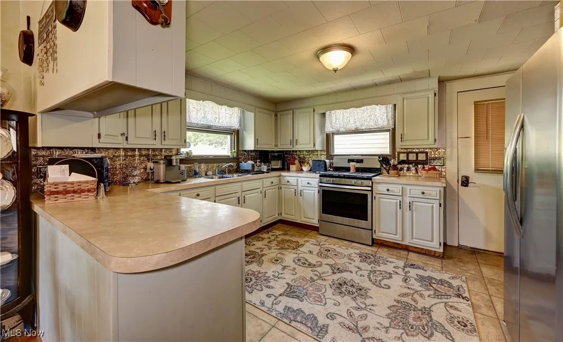 Kitchen featuring stainless steel appliances, a peninsula, decorative backsplash, light countertops, and light tile patterned floors