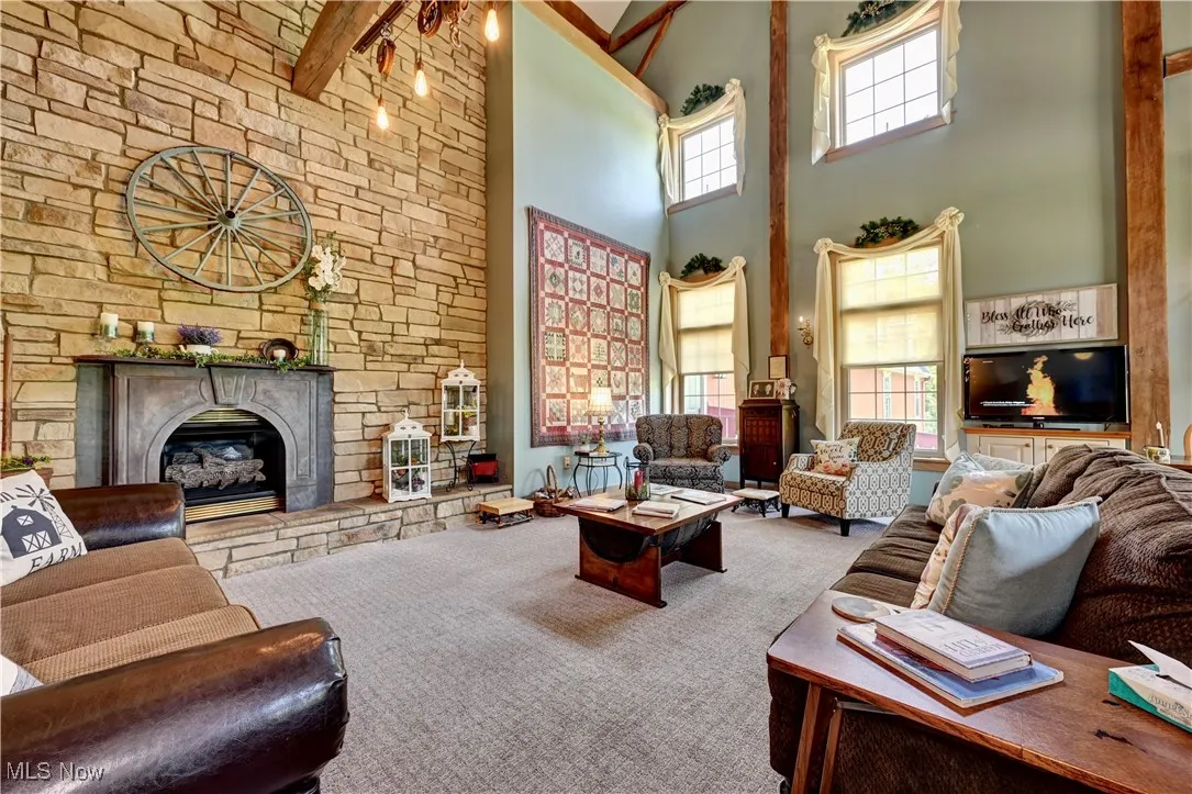 Carpeted living area featuring a towering ceiling, a fireplace, and beamed ceiling