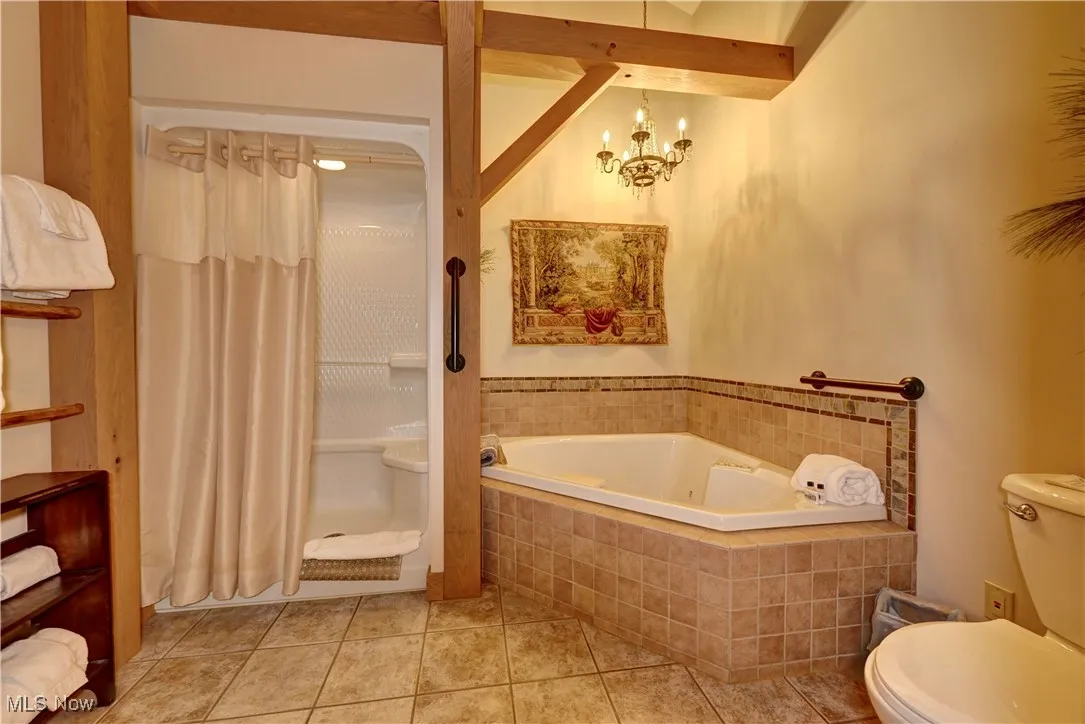 Full bathroom featuring toilet, a tub with jets, tile patterned flooring, curtained shower, and a chandelier