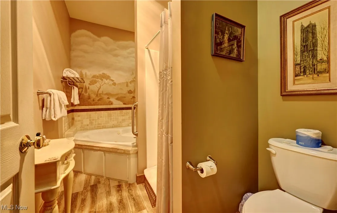 Bathroom featuring wood finished floors, toilet, a bath, and curtained shower