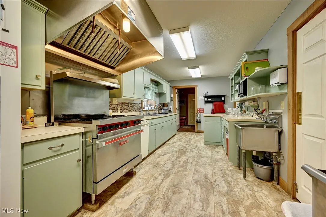 Kitchen featuring green cabinetry, a sink, light countertops, premium stove, and open shelves