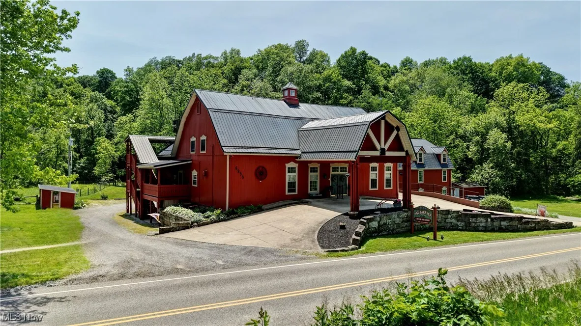 View of front of home with metal roof, a gambrel roof, a view of trees, concrete driveway, and a front lawn