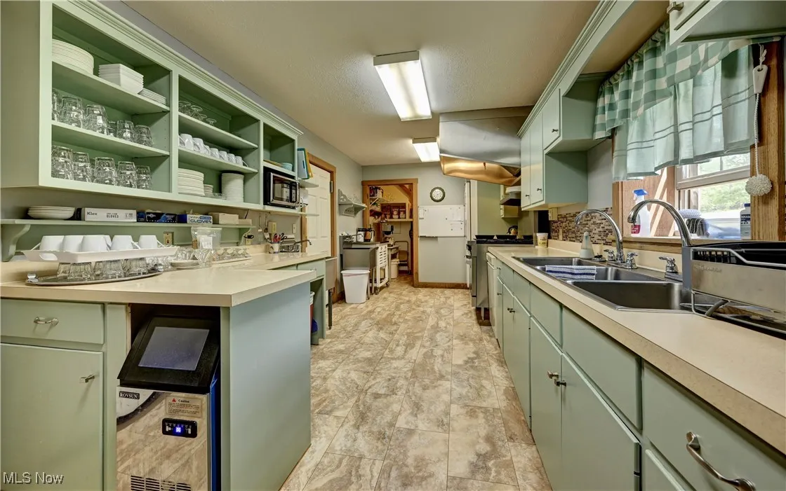 Kitchen with green cabinetry, stainless steel range oven, a sink, stone finish floors, and light countertops
