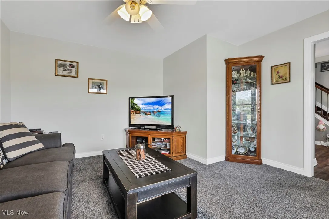 Carpeted living room with ceiling fan and baseboards