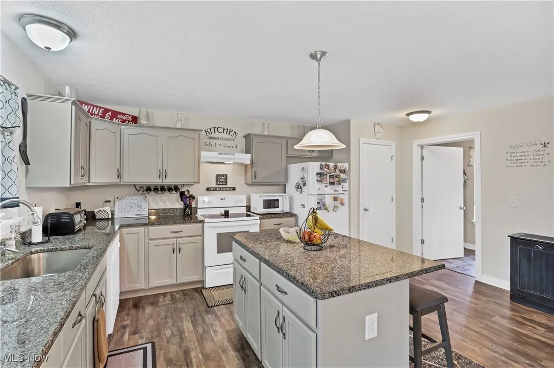 Kitchen featuring white appliances, a sink, under cabinet range hood, and dark wood-style floors
