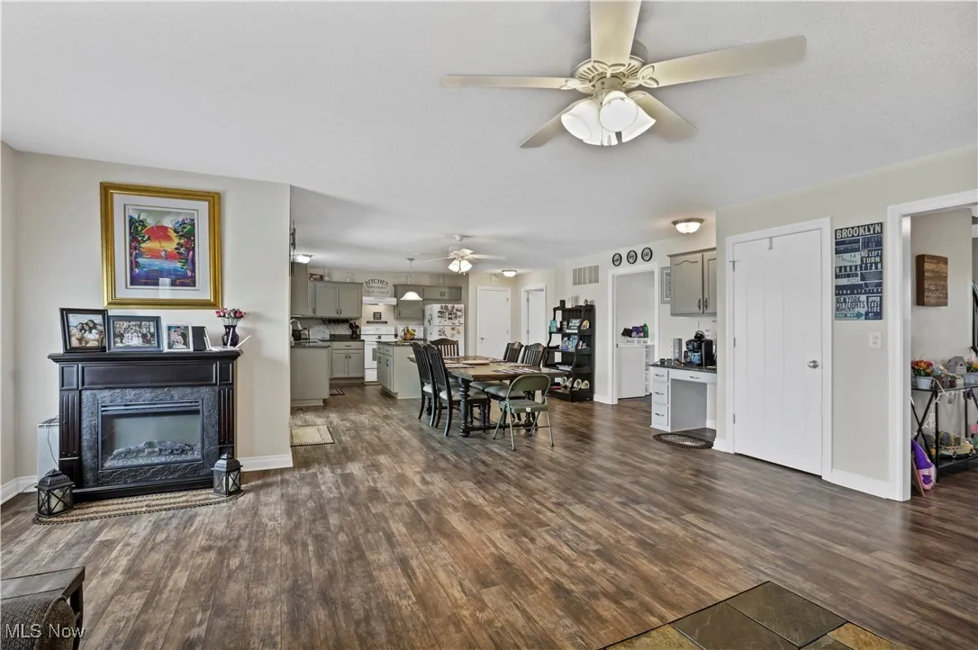 Living room featuring dark wood-style floors, a ceiling fan, a glass covered fireplace, and baseboards