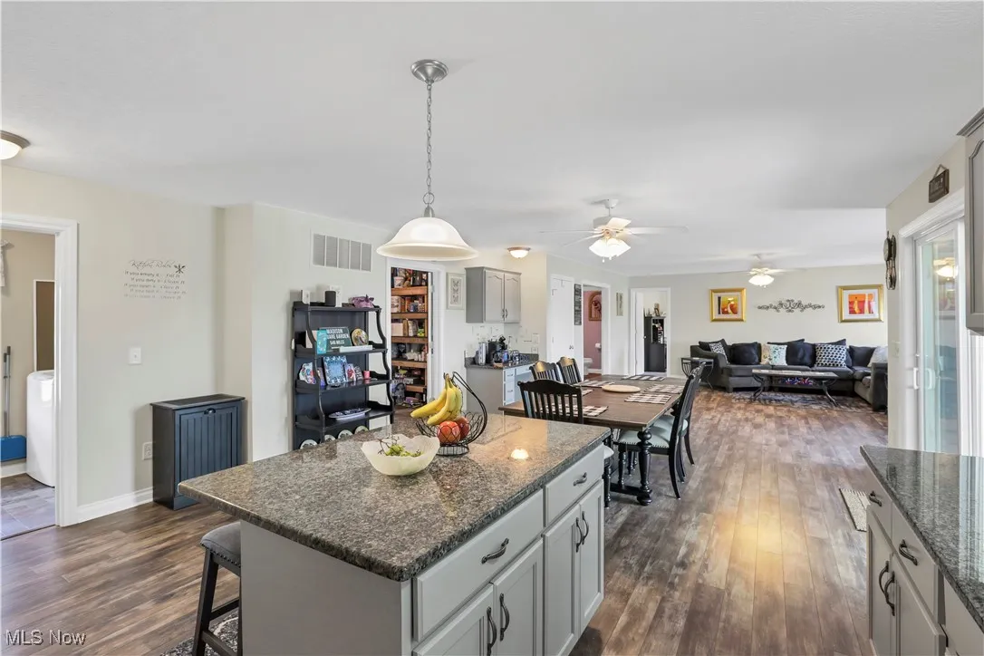 Kitchen with dark wood-style flooring, a kitchen island, a ceiling fan, a kitchen breakfast bar, and gray cabinets