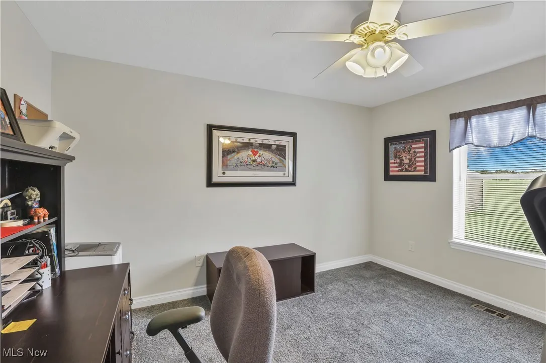 Carpeted office space featuring a ceiling fan and baseboards