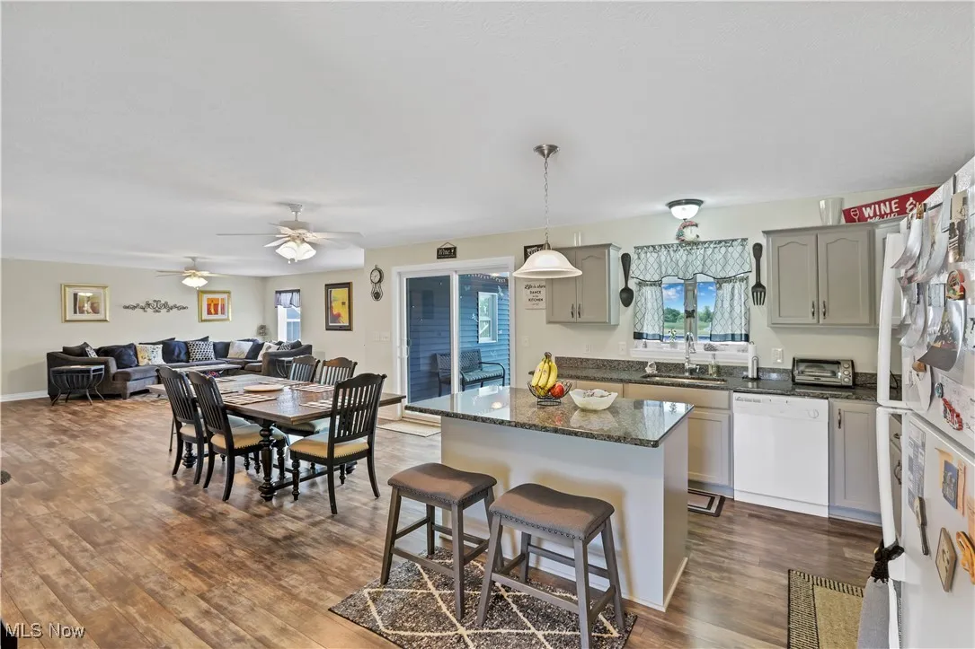Kitchen featuring white appliances, a sink, a kitchen island, dark wood finished floors, and a kitchen breakfast bar