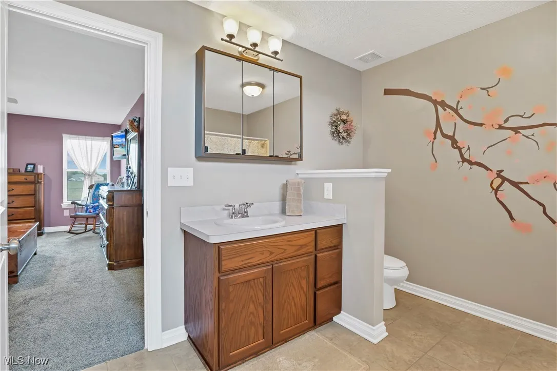 Bathroom featuring vanity, toilet, baseboards, and a textured ceiling
