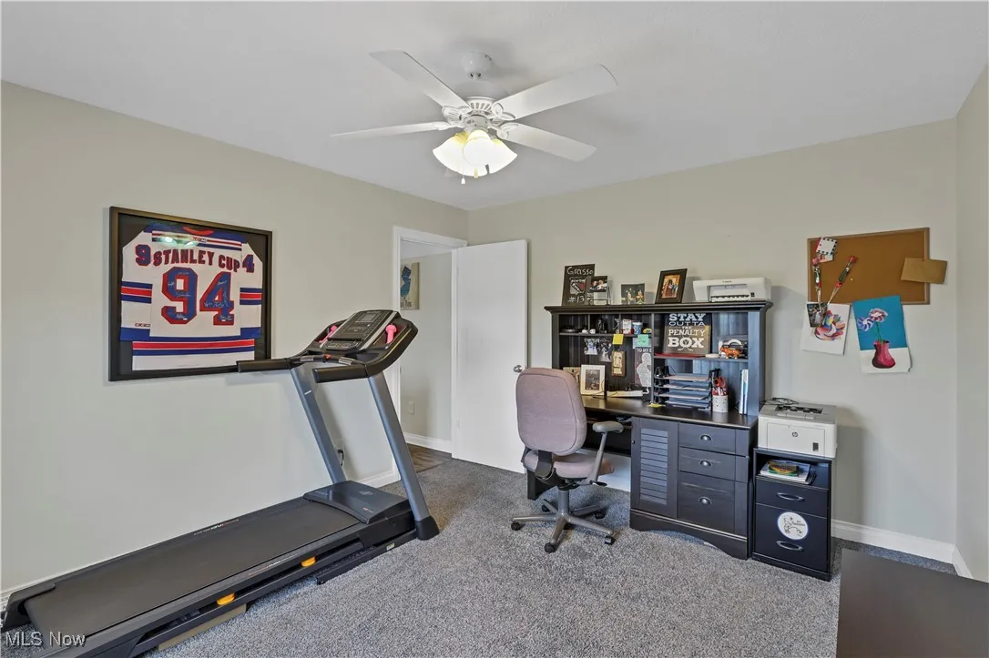Office space featuring baseboards, dark colored carpet, and ceiling fan