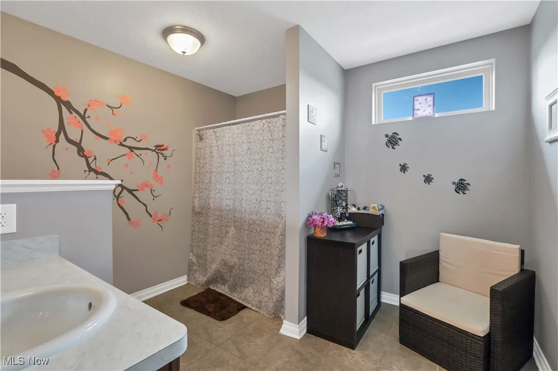 Bathroom with vanity, curtained shower, baseboards, and tile patterned flooring
