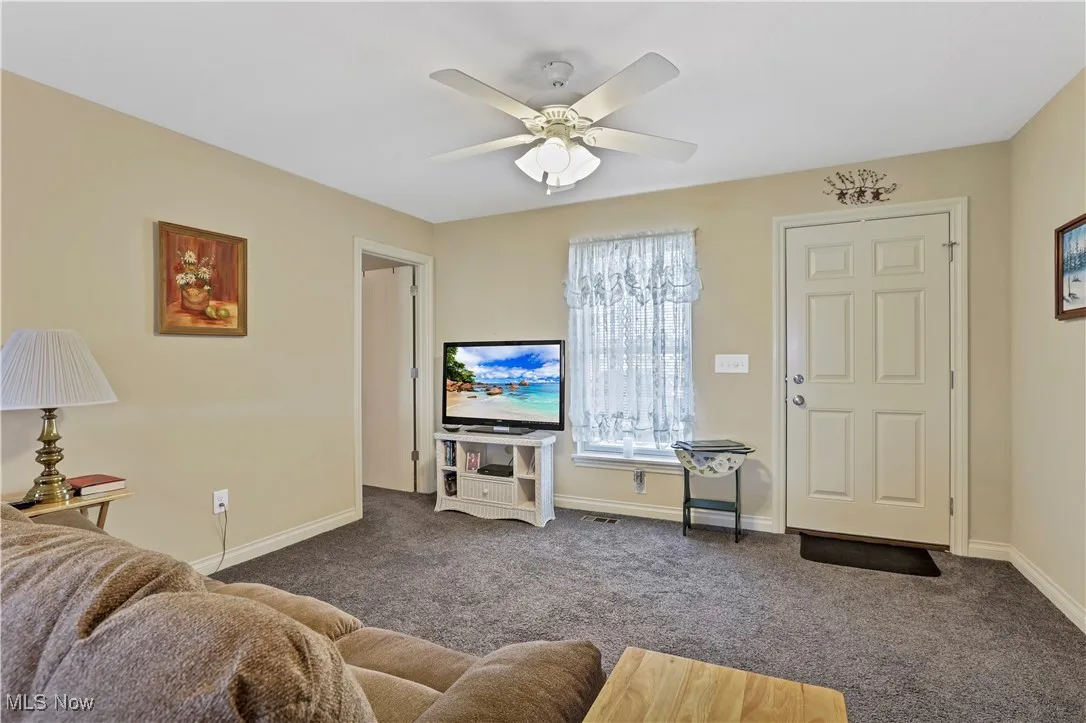 Living area with ceiling fan, dark carpet, and baseboards