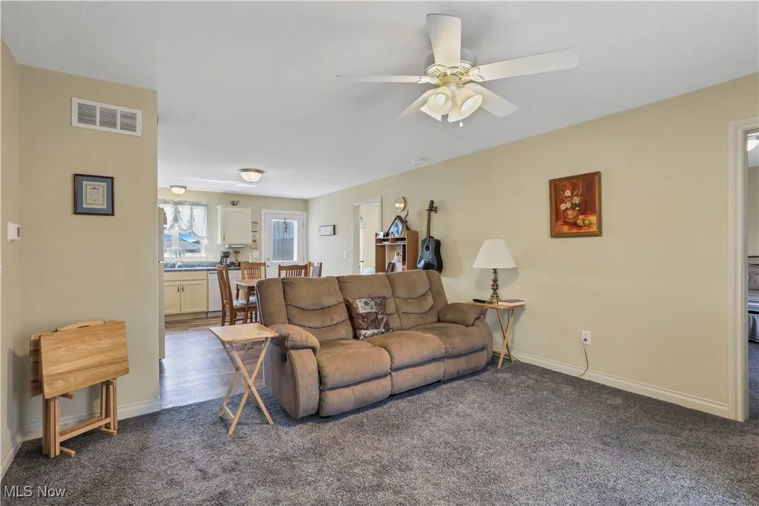 Living room with dark carpet, ceiling fan, and baseboards