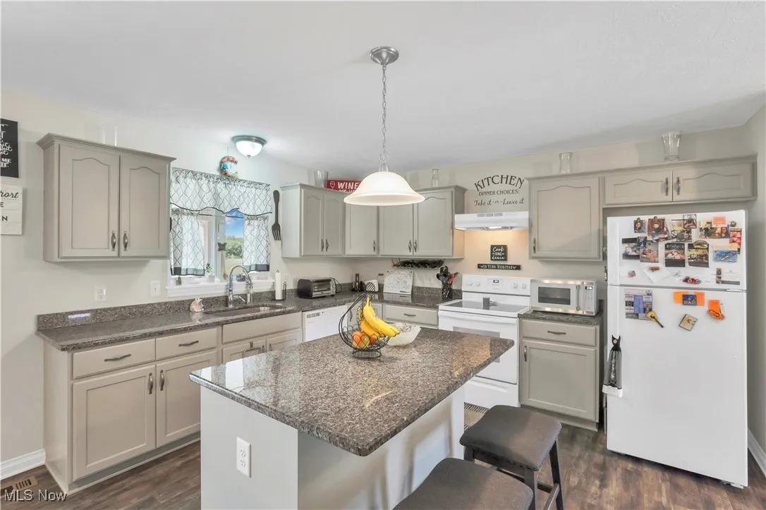 Kitchen featuring white appliances, under cabinet range hood, a sink, a kitchen breakfast bar, and gray cabinets
