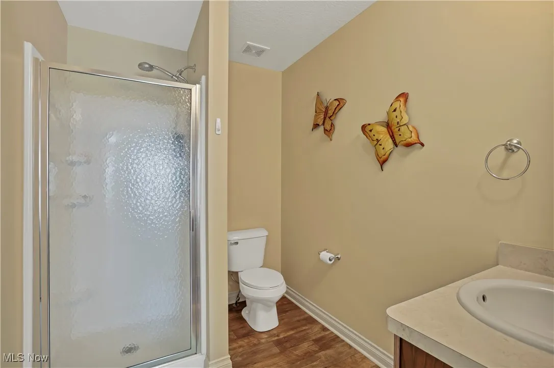 Bathroom with wood finished floors, a shower stall, vanity, toilet, and baseboards