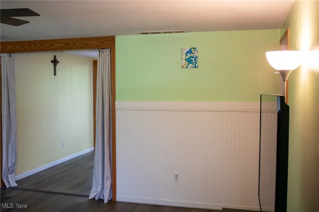 Spare room with wainscoting, dark wood-style flooring, and a ceiling fan
