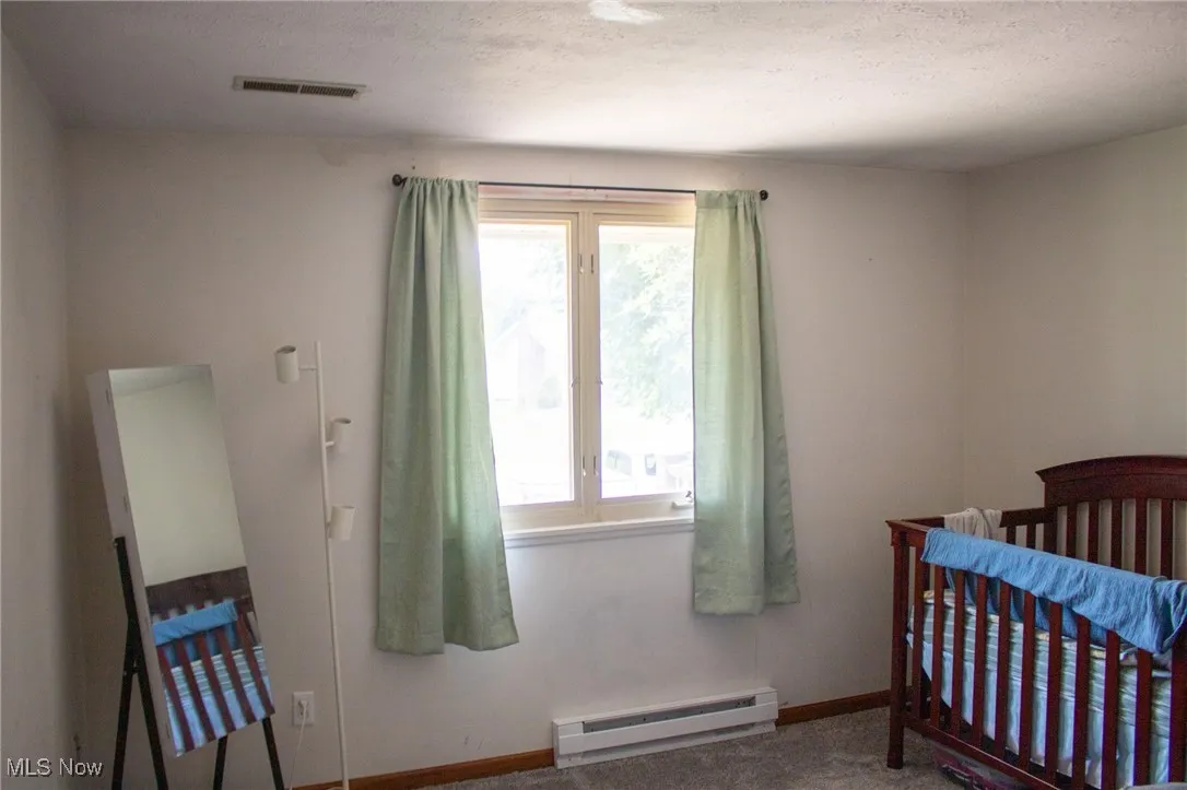 Bedroom featuring a baseboard radiator, a crib, and a textured ceiling