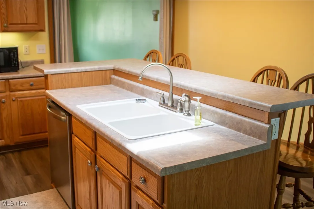 Kitchen featuring a kitchen breakfast bar, black microwave, dishwasher, brown cabinets, and dark wood-style floors