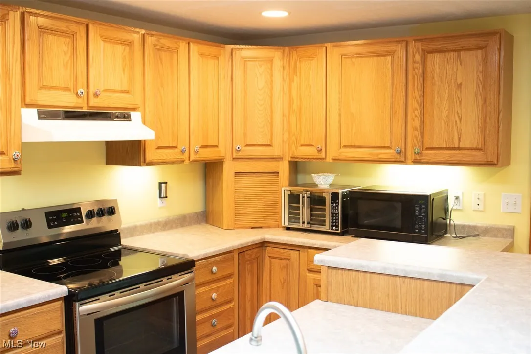 Kitchen with stainless steel electric range, under cabinet range hood, light countertops, black microwave, and recessed lighting