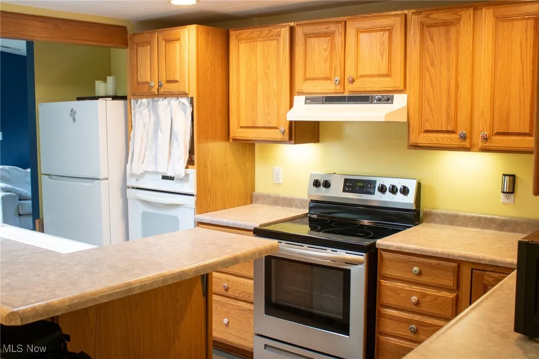 Kitchen featuring under cabinet range hood, stainless steel electric stove, freestanding refrigerator, and light countertops