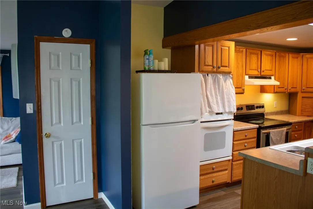 Kitchen with white appliances, under cabinet range hood, dark wood finished floors, light countertops, and a sink