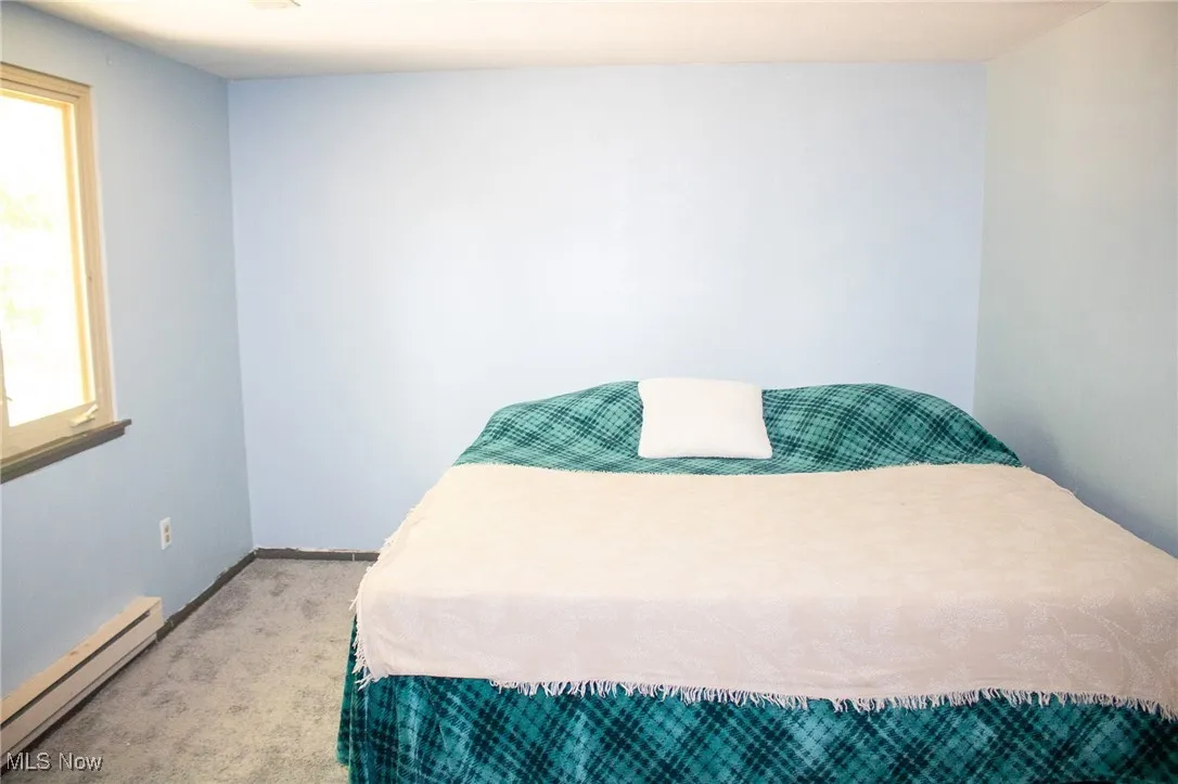 Bedroom featuring baseboard heating, multiple windows, and light colored carpet
