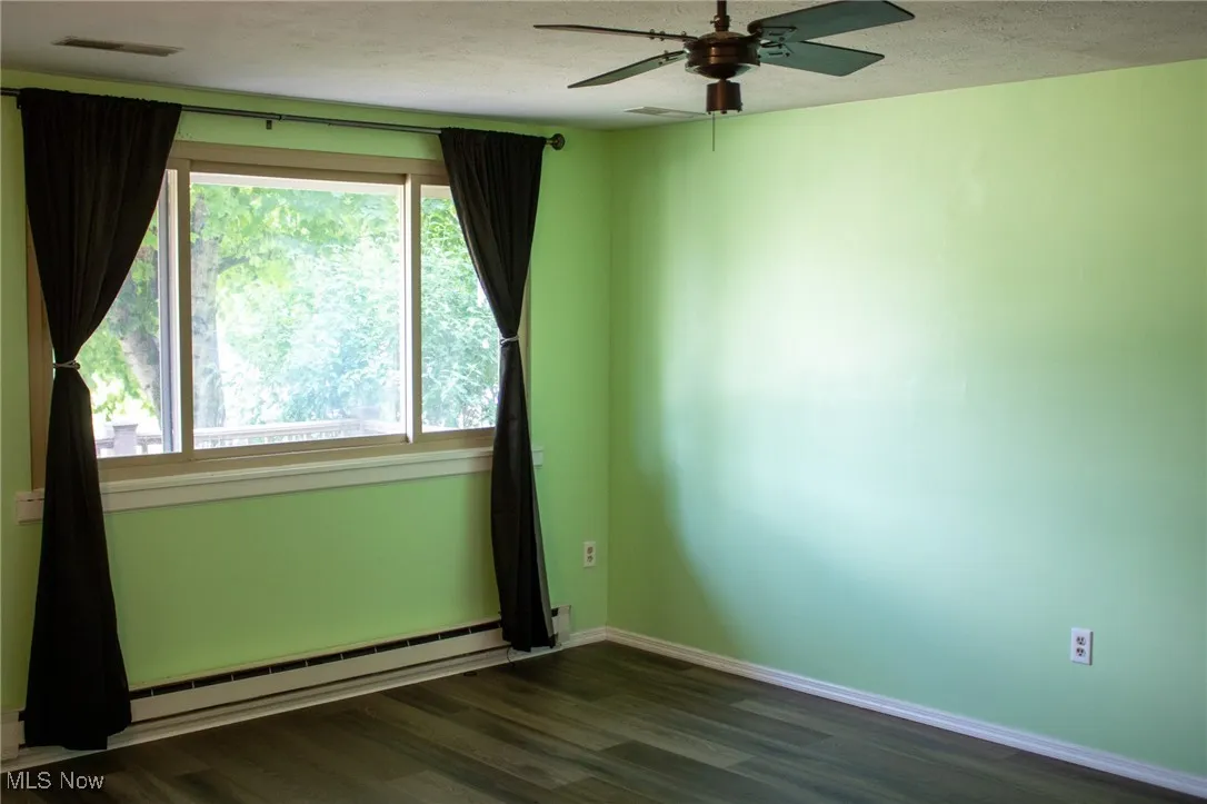 Spare room featuring a baseboard radiator, dark wood-style flooring, healthy amount of natural light, ceiling fan, and a textured ceiling