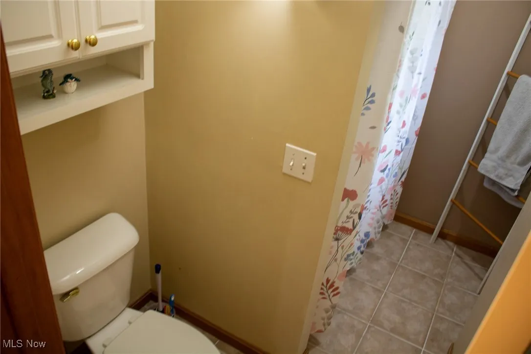 Full bath featuring toilet, curtained shower, baseboards, and tile patterned floors